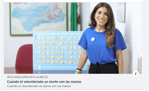 Imagen de Laura, voluntaria de ASOCIDE Andalucía, de pie, al lado de una mesa, en el despacho de ASOCIDE en Sevilla. De fondo se ve un cartel del dactilológico de lengua de signos y en palma